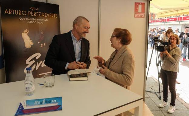 Arturo Pérez-Reverte charla con una lectora en la caseta de firmas de la Plaza Mayor. /G. Villamil